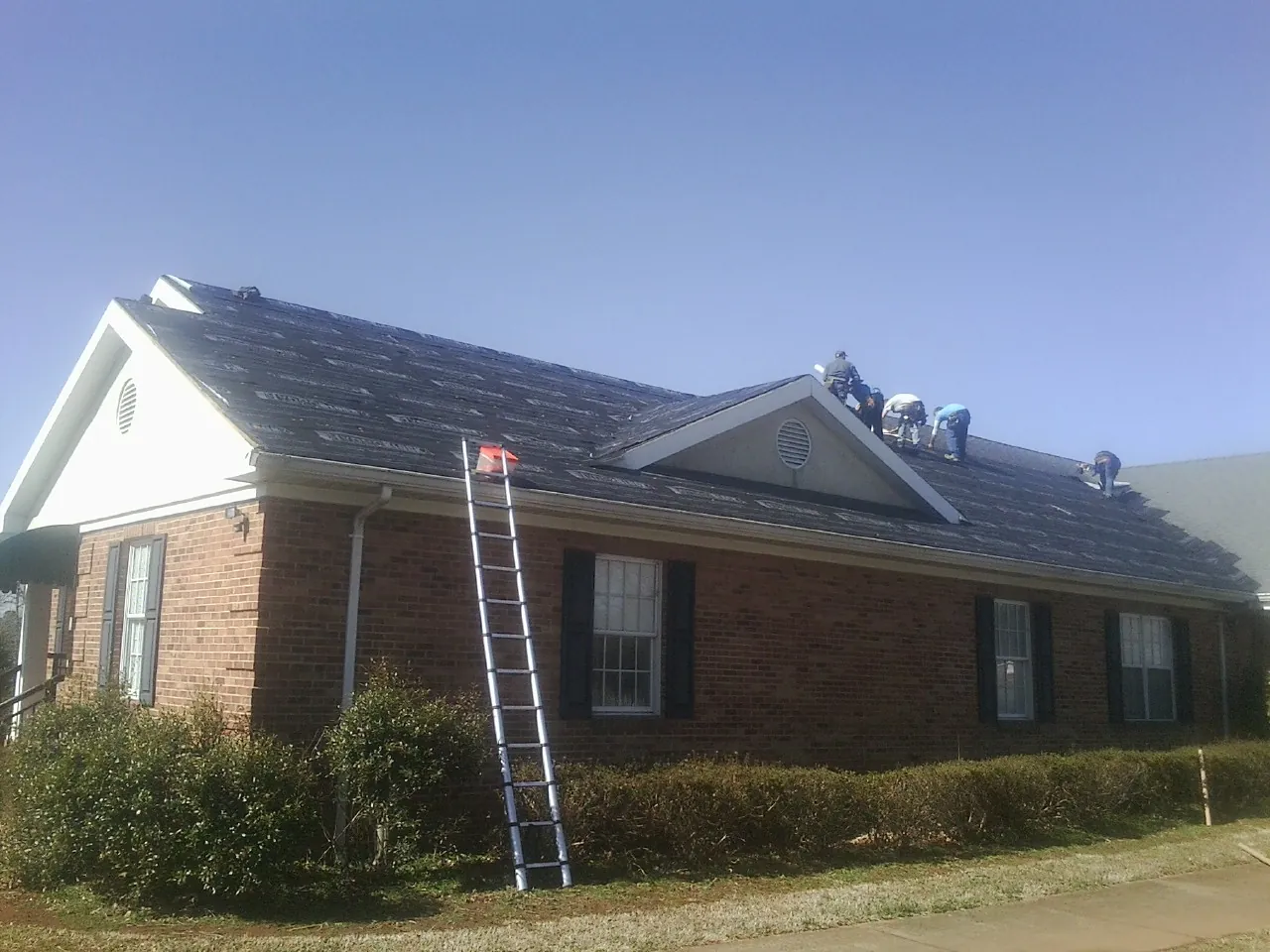 Crew tearing shingles off a brick ranch roof with a ladder set — Metal Roof Repair work by our crew in Castle Rock