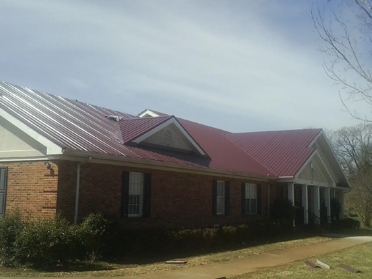 Red metal roof with gabled entries on a long brick building, from a Hail Damage Roof Repair job in Castle Rock