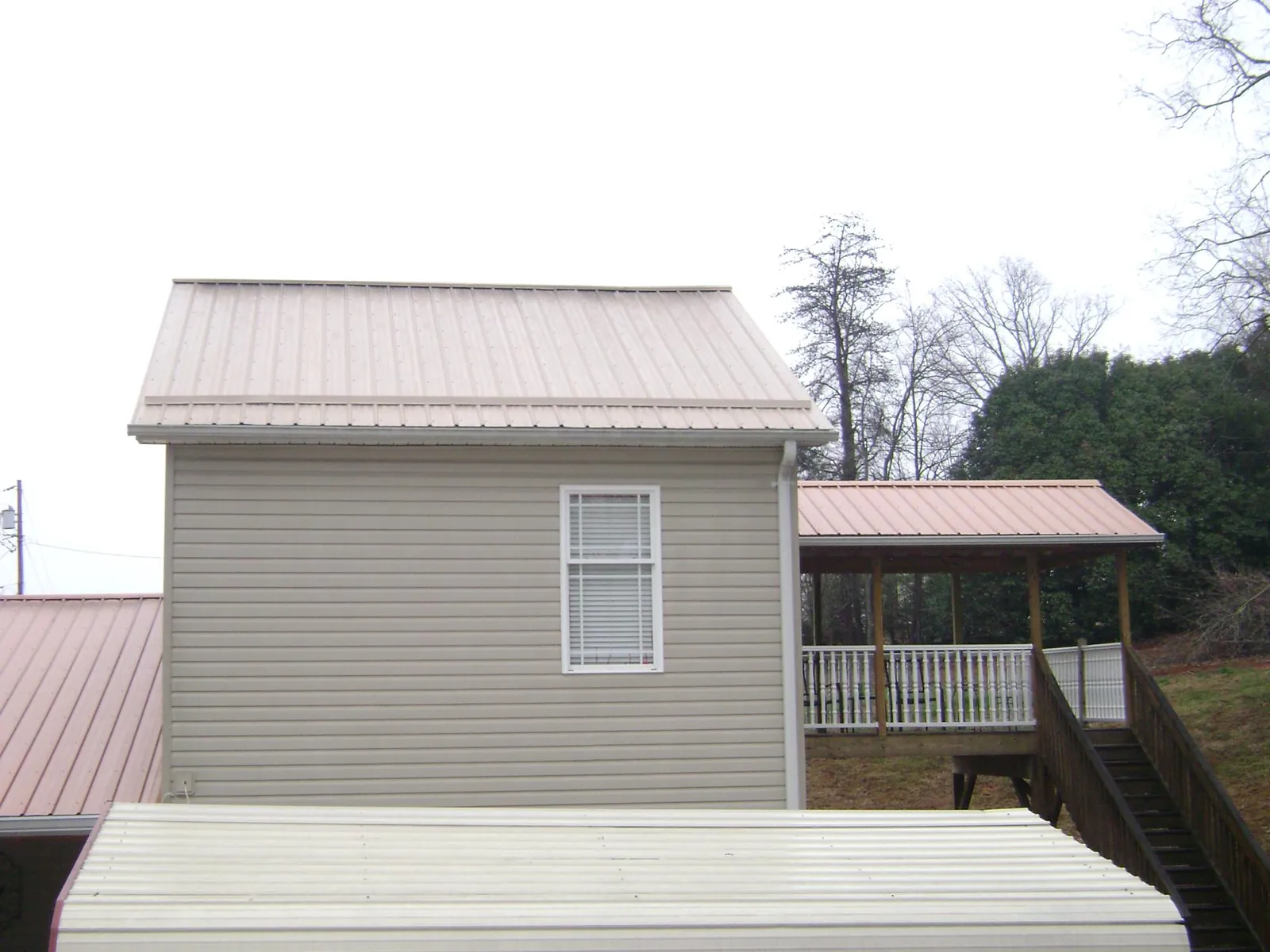 Tan metal roofs on a two story addition and attached porch, from a Roof Replacement job in Castle Rock